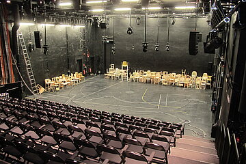 Blick auf die Bühne im BE aus der rechten hinteren Ecke des Raumes über die Stuhlreihen hinweg.