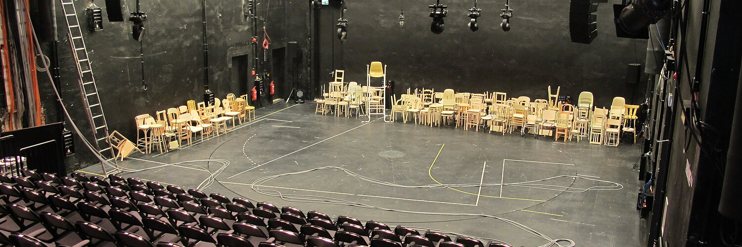 Blick auf die Bühne im BE aus der rechten hinteren Ecke des Raumes über die Stuhlreihen hinweg.