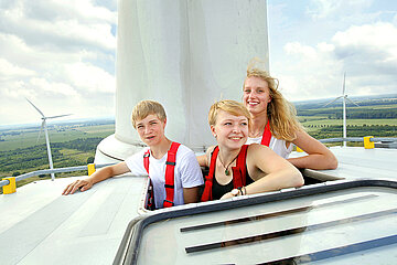 Drei Jugendliche schauen aus einer Öffnung oben auf einem Windkraftrad.